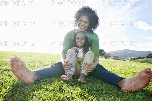 Portrait of smiling mixed race mother and daughter sitting in grass