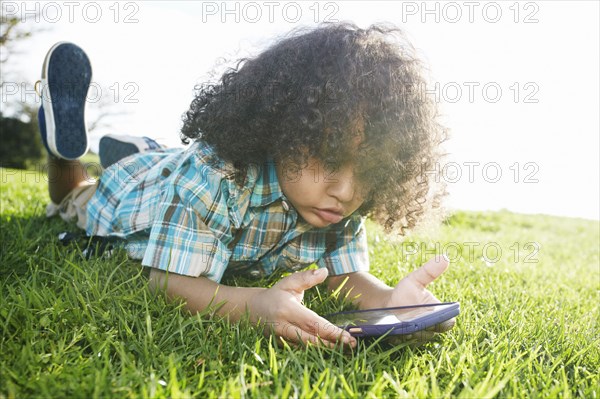 Mixed race boy laying in grass holding cell phone