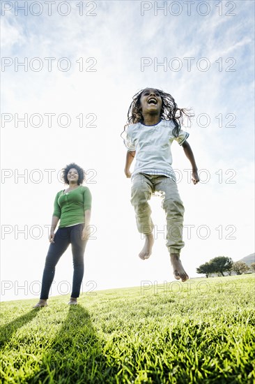 Mixed race mother watching daughter jumping in the grass