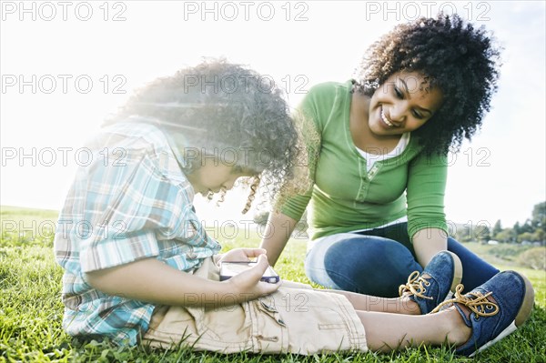 Mixed race mother watching son use cell phone in grass