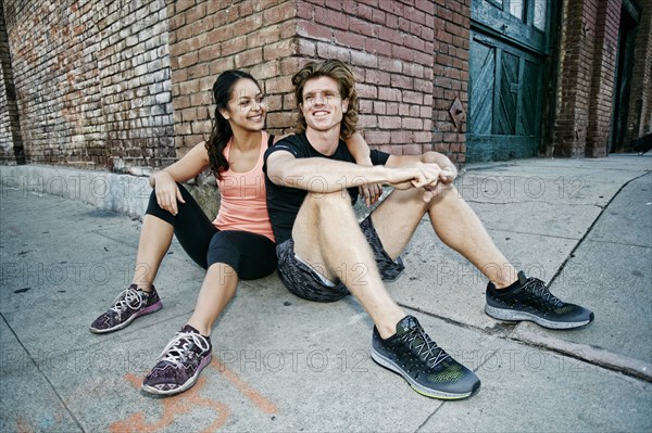 Couple sitting on sidewalk leaning on corner of brick building