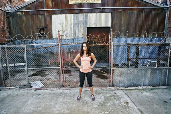 Confident mixed race woman standing on sidewalk near barbed-wire fence