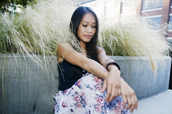 Pensive Asian woman sitting near foliage