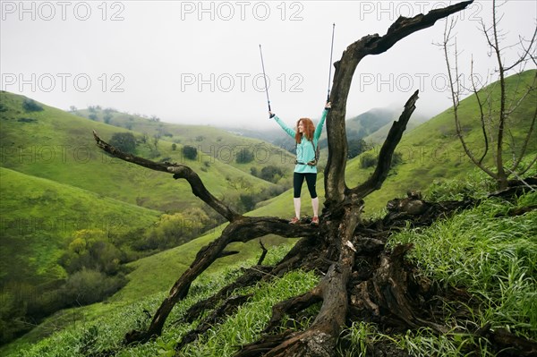 Caucasian woman standing on tree celebrating with walking sticks