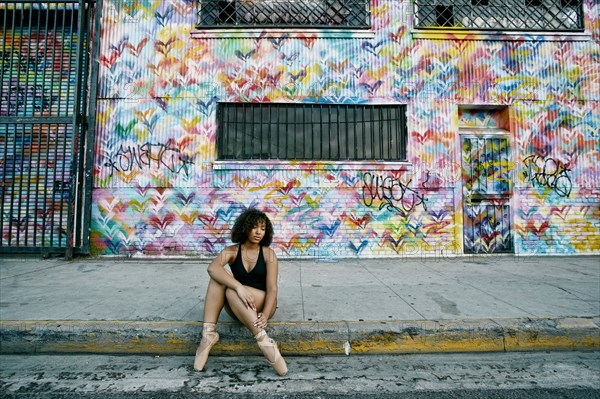 Mixed race ballet dancer sitting on curb rubbing leg