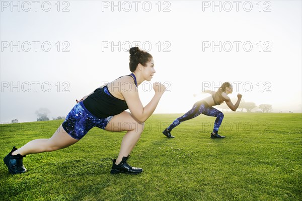 Mixed race women stretching legs in field