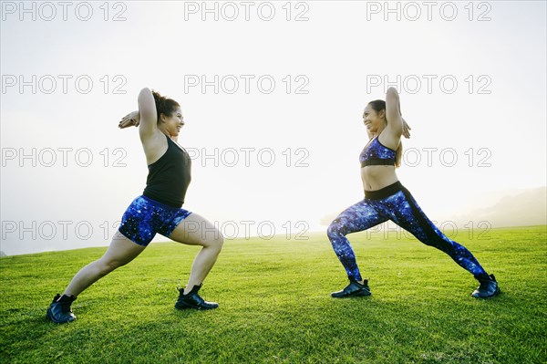 Mixed race women stretching arms in field