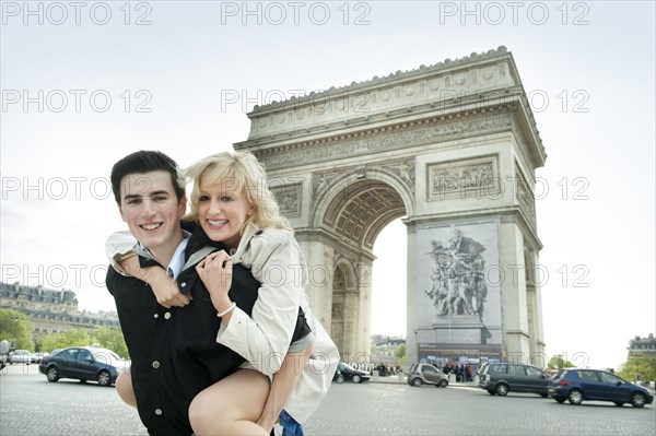 Caucasian man giving girlfriend piggyback ride near Arc de Triomphe