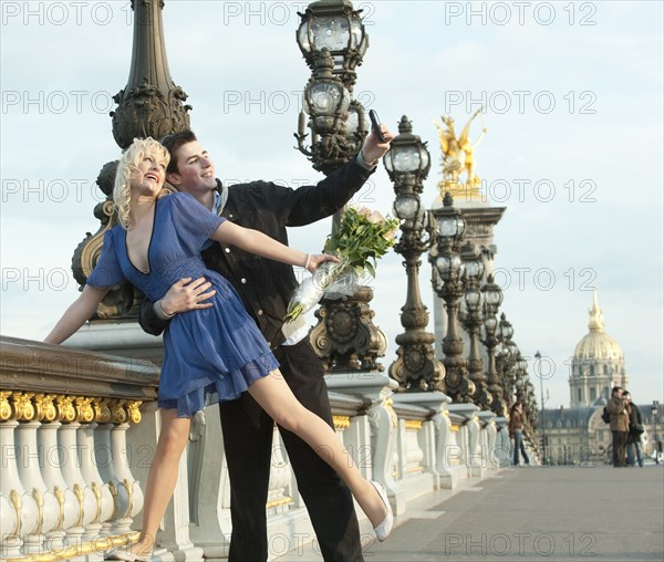 Caucasian couple taking self-portrait on bridge