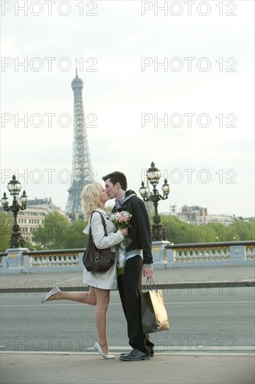 Caucasian couple kissing on bridge with Eiffel Tower in background
