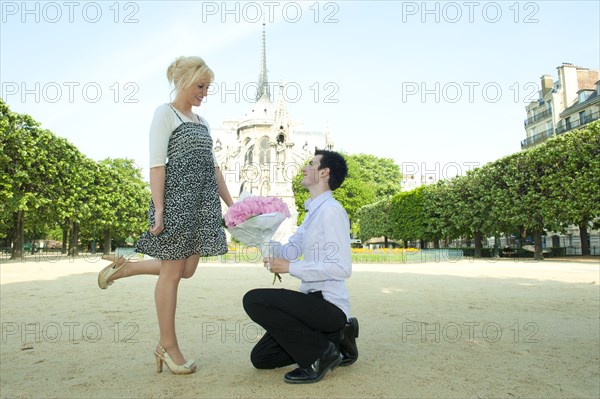 Caucasian man proposing to girlfriend in park near Notre Dame