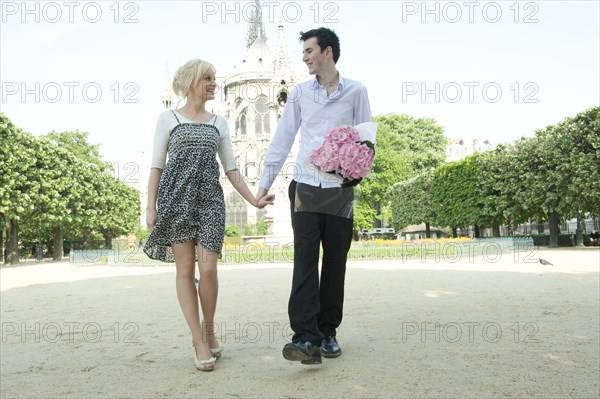 Caucasian couple holding hands in park near Notre Dame