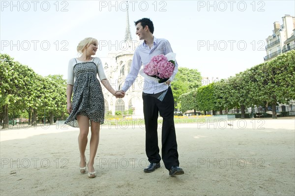 Caucasian couple holding hands in park near Notre Dame