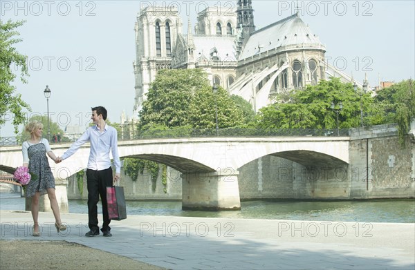 Caucasian couple walking along city river near Notre Dame