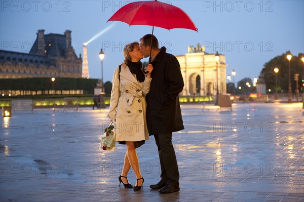 Caucasian couple kissing in rain at night near the Louvre
