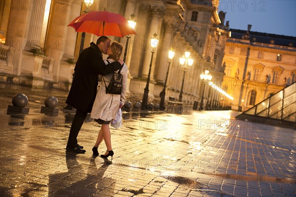 Caucasian couple kissing in rain at night at the Louvre