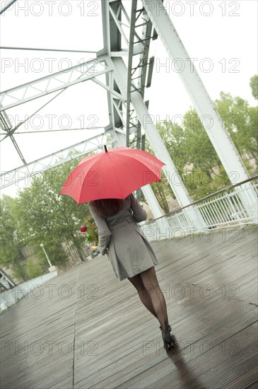 Caucasian woman walking in rain with red umbrella