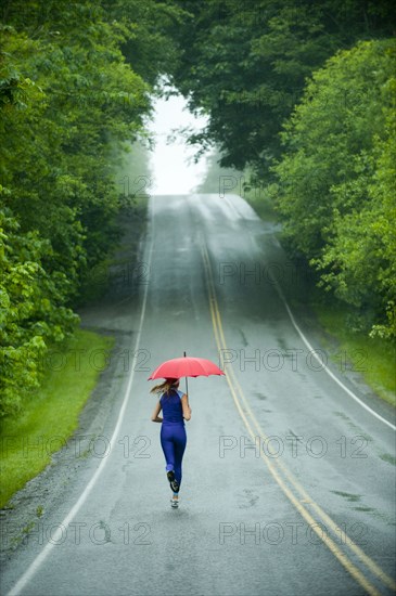 Caucasian woman running on remote road with umbrella