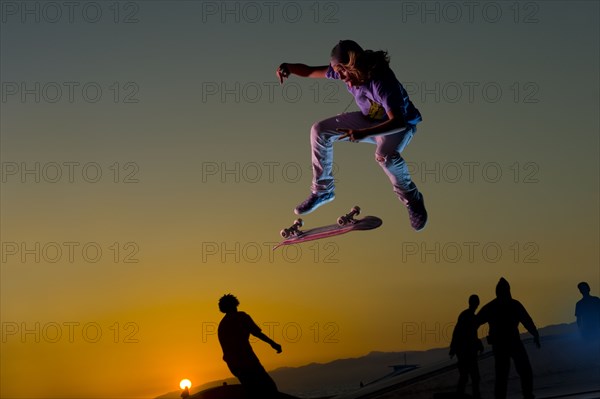 Skateboarder doing stunt in mid-air at sunset