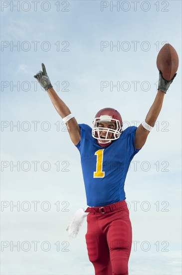 Mixed race football player with arms raised holding football