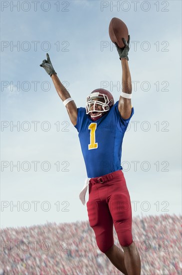 Mixed race football player with arms raised holding football