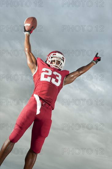 African American football player with arms raised holding football