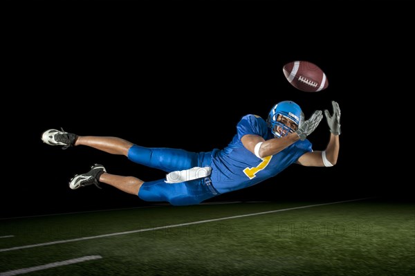 Mixed race football player jumping in mid-air catching football