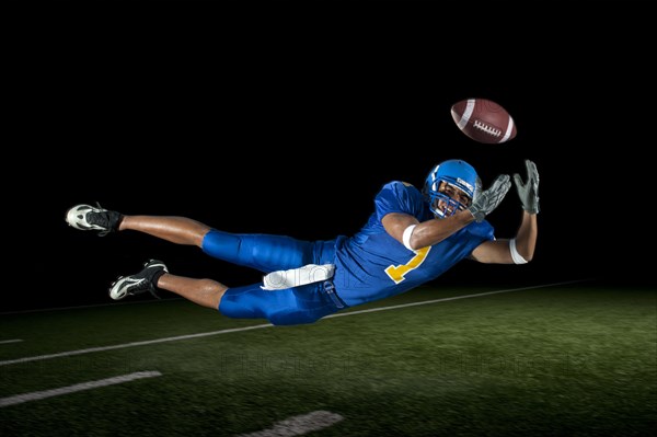 Mixed race football player jumping in mid-air catching football