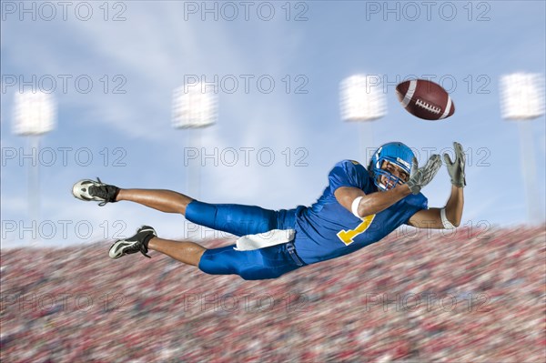 Mixed race football player jumping in mid-air catching football