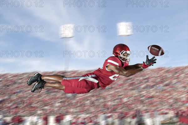 African American football player jumping in mid-air catching football