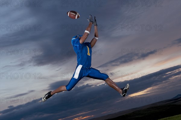 Mixed race football player jumping in mid-air catching football