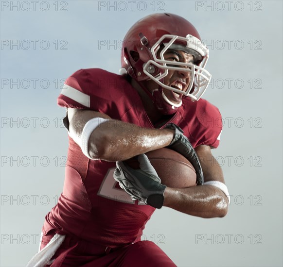 Grimacing Black football player carrying football