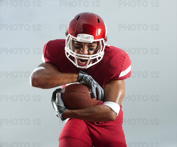 Grimacing Black football player carrying football