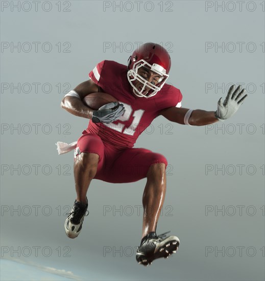 Grimacing Black football player carrying football in mid-air