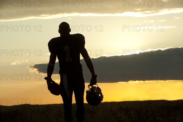 Silhouette of Black football player carrying helmet and football