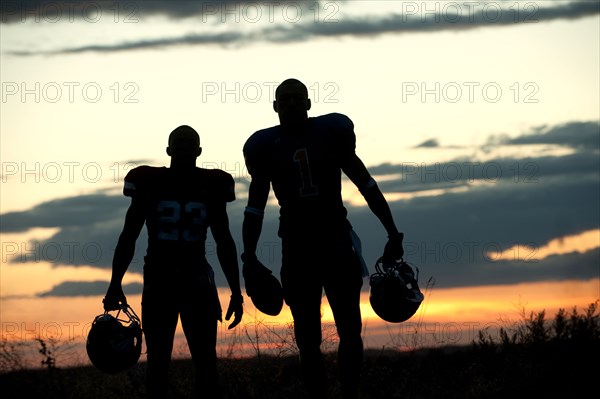 Silhouette of Black football players carrying helmet and football