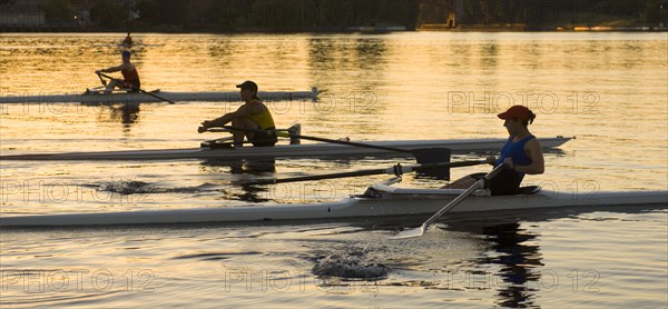 People rowing sculling boats on river