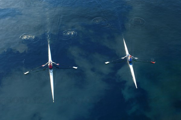 People rowing sculling boats on river