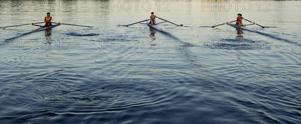 People rowing sculling boats on river