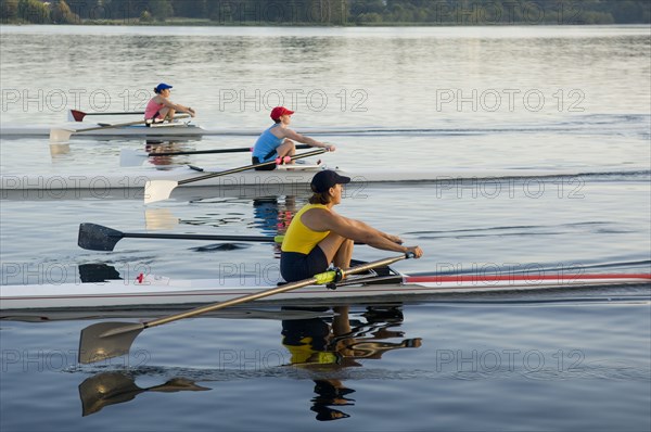 People rowing sculling boats on river