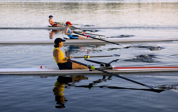People rowing sculling boats on river