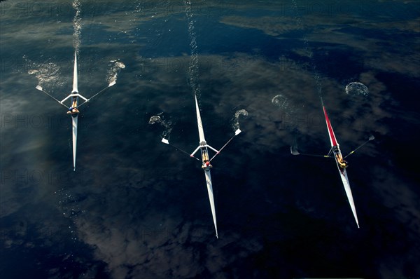 People rowing sculling boats on river