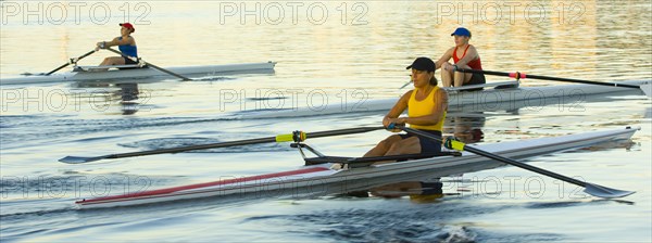 People rowing sculling boats on river