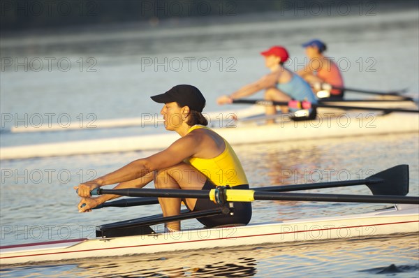 People rowing sculling boats on river