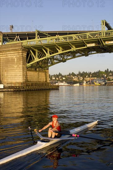 Person rowing sculling boat on river under bridge