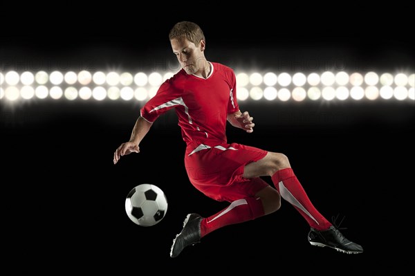 Soccer player jumping in mid-air kicking ball at night