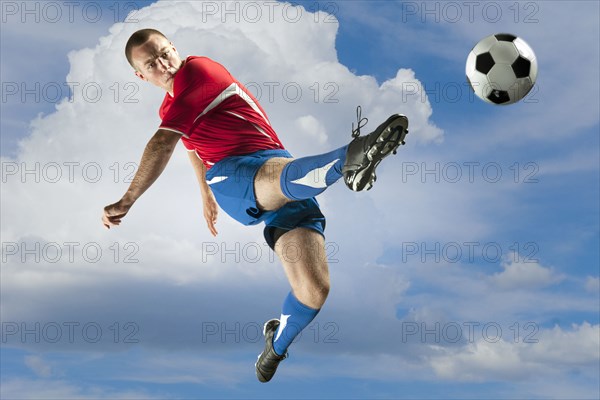 Soccer player jumping in mid-air kicking ball