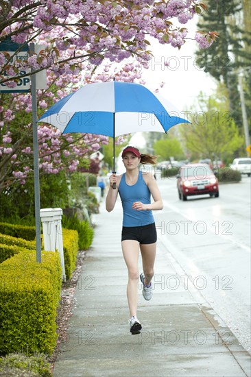 Mixed race runner training on urban sidewalk with umbrella