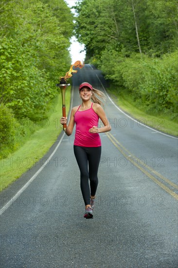 Caucasian athlete running with Olympic torch on remote road
