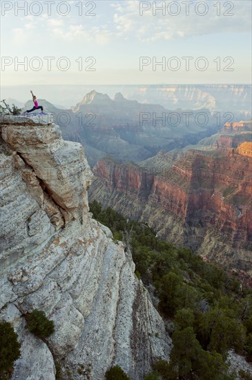 Caucasian woman practicing yoga on cliff near canyon